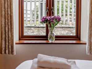 A window with a wooden frame, a clear view of a stone wall, and a vase with purple flowers on a bedside table. - 4 Bed in Launceston (oc-brhig) (Launceston)