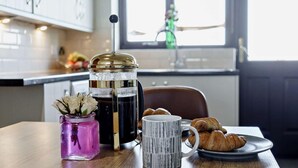 Een keuken met een koffiezetapparaat, een vaas met bloemen, een mok en croissants op een bord.