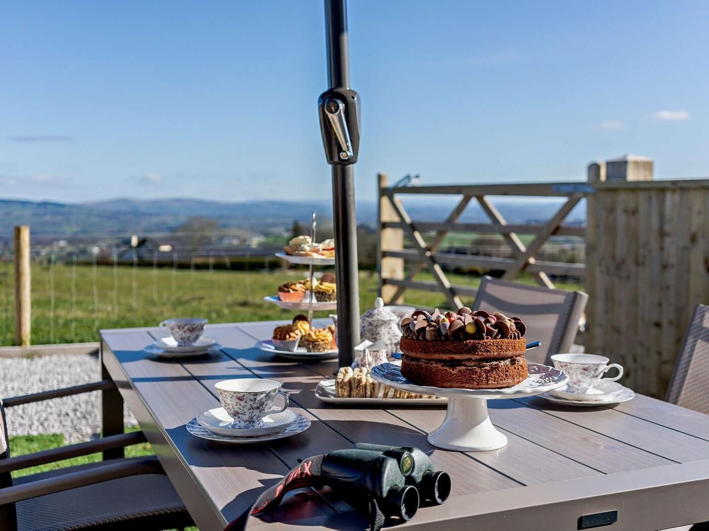 Une table dressée à l’extérieur, avec un gâteau, des tasses à thé et des jumelles, par une journée ensoleillée.