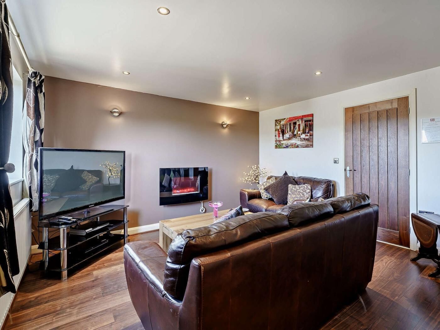 Een woonkamer met een leren bank, een flatscreen televisie, een salontafel en een houten deur.