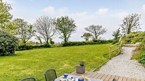 Ein Tisch im Freien mit Stühlen, einem kleinen Topfpflanzen und Blick auf eine Wiese mit Bäumen.