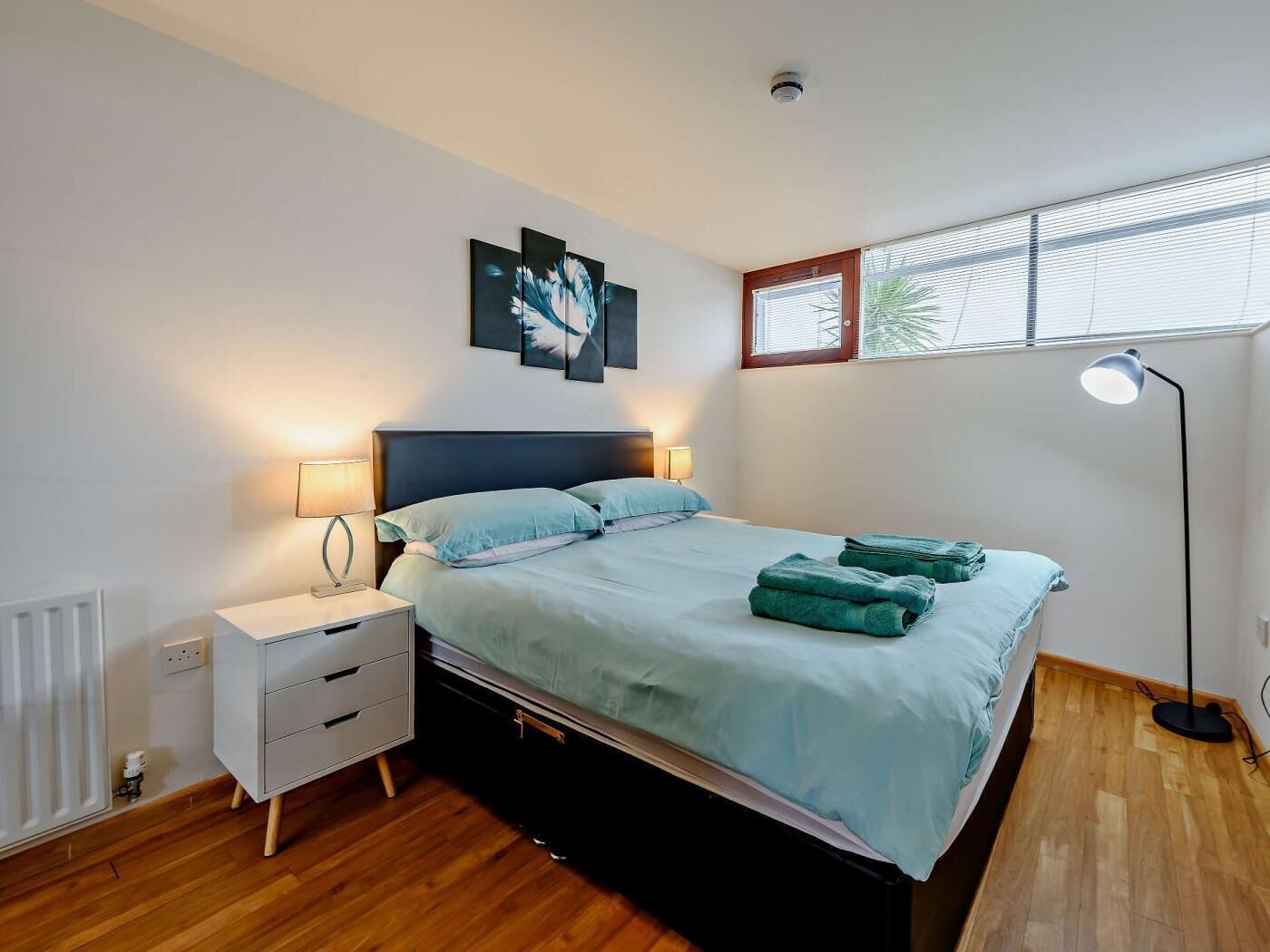 A bedroom with a bed, bedside tables, a floor lamp, and a window with blinds.