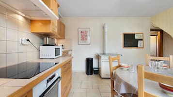Een keuken met houten kastjes, een magnetron, een oven, een spoelbak en een eethoek met een tafel en stoelen.