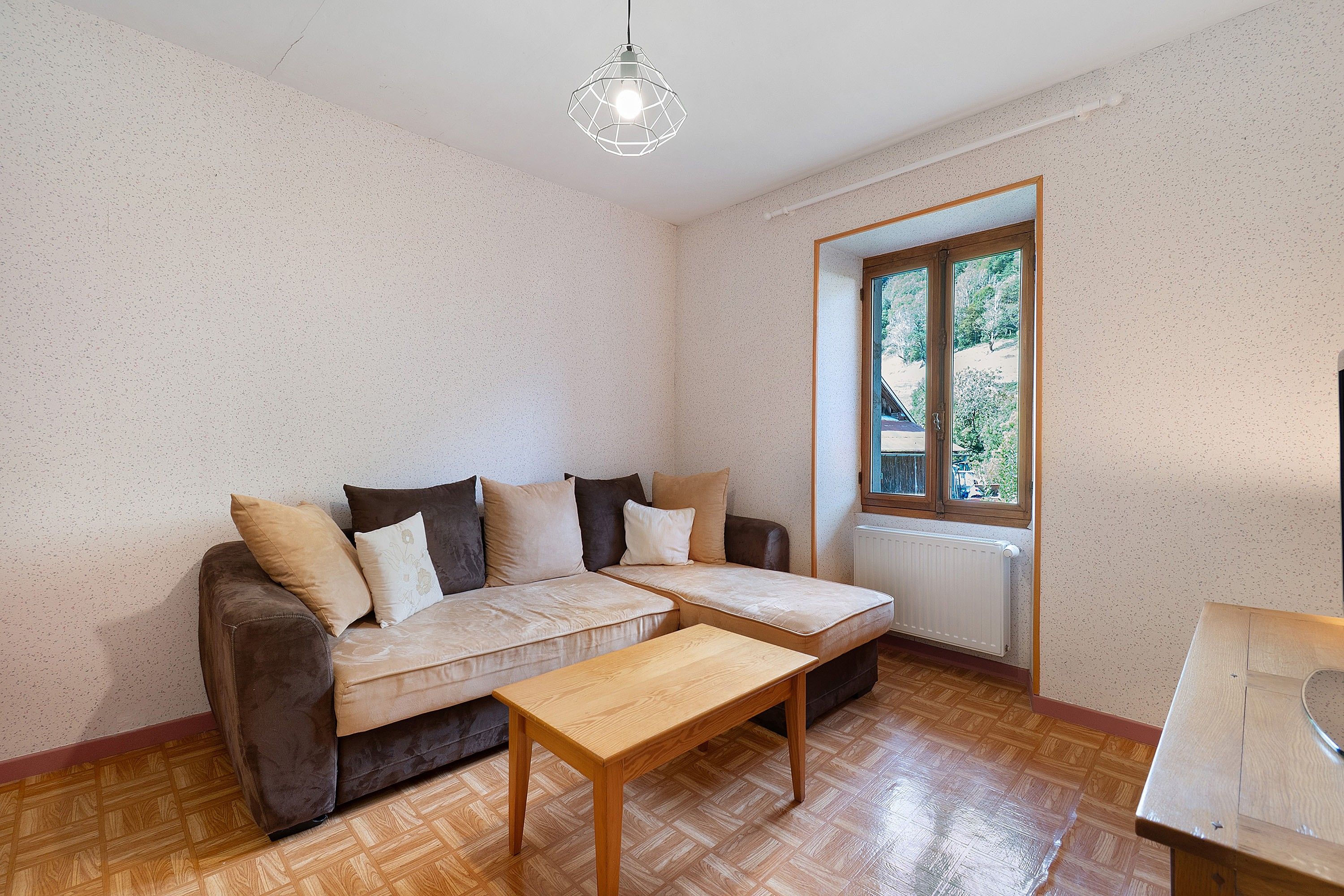 A room with a sofa, a wooden table, and a window with a view of greenery.