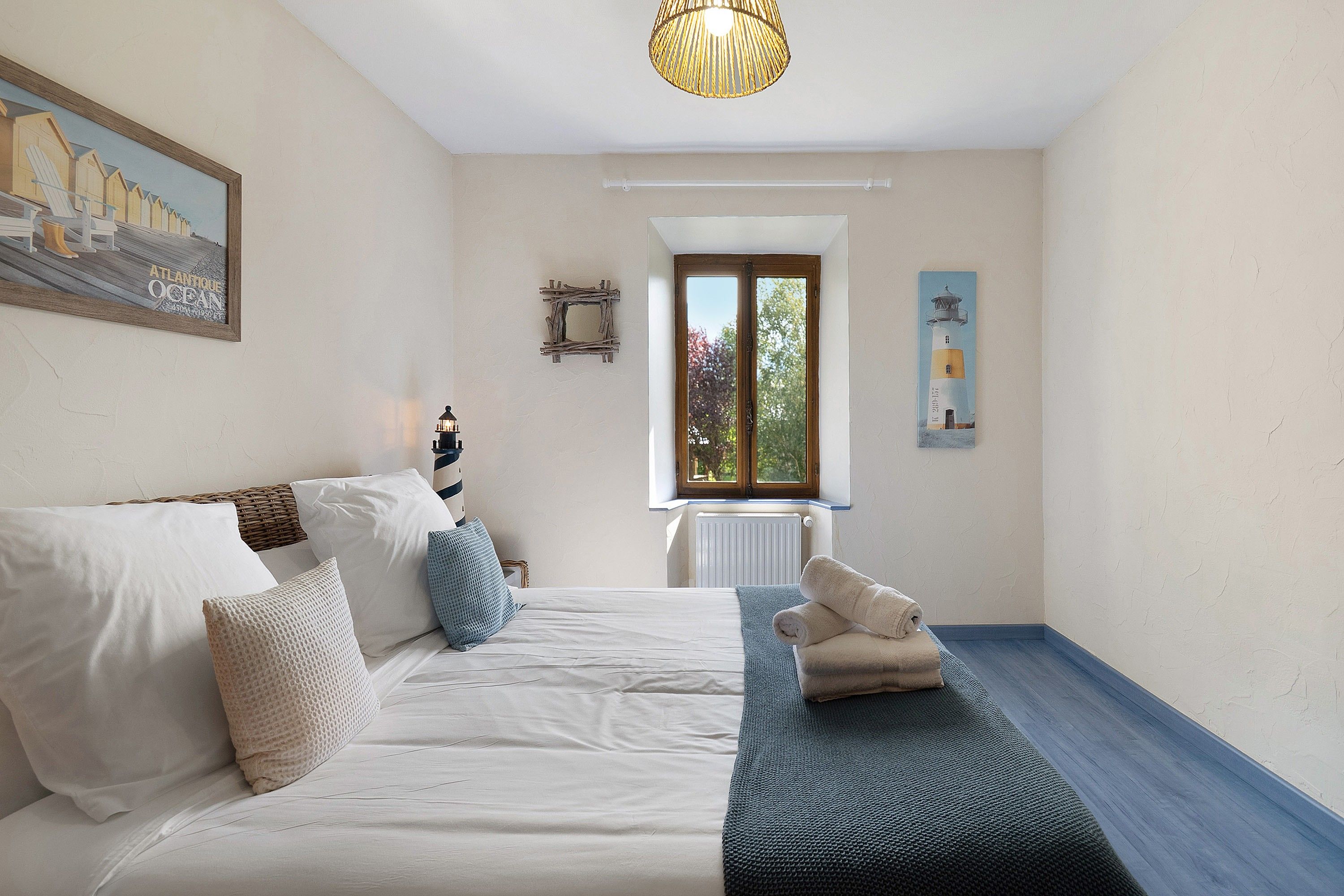 A bedroom with a bed, a window, a painting, and a lamp.