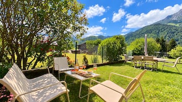 Een terras met stoelen en een tafel, een fles wijn en een schaal fruit.