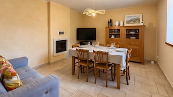 Een eethoek met een tafel voor vier personen, een televisie, een open haard en een kast met glazen deuren.