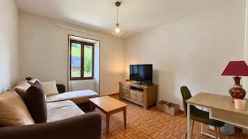 Et møbleret værelse med sofa, fjernsyn, spisebord og et vindue med udsigt til grønne omgivelser.