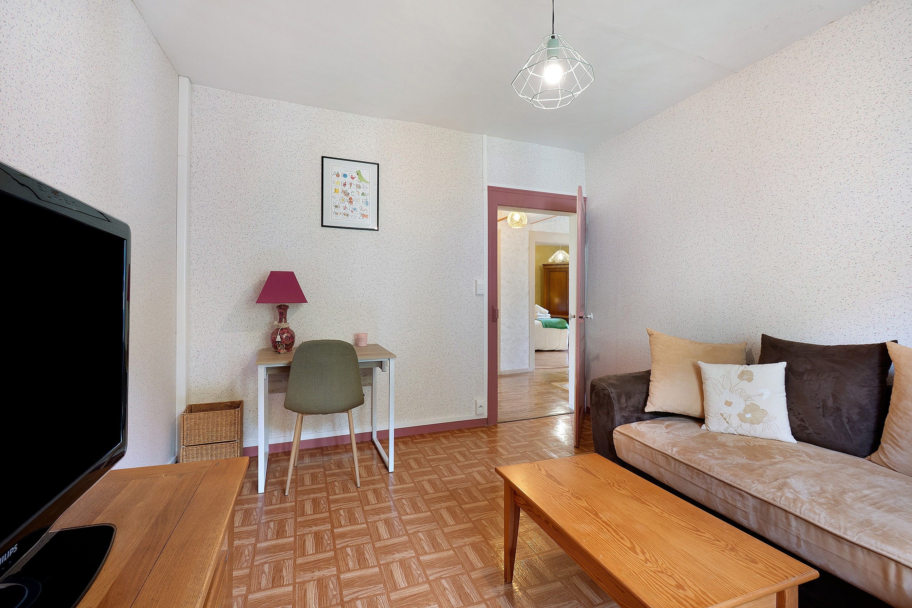 Ein Wohnzimmer mit Sofa, Couchtisch, Fernseher, Lampe, Sessel und einem gerahmten Bild an der Wand.