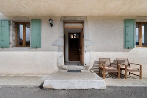 Un edificio con fachada de hormigón, puerta de madera y contraventanas verdes en las ventanas.