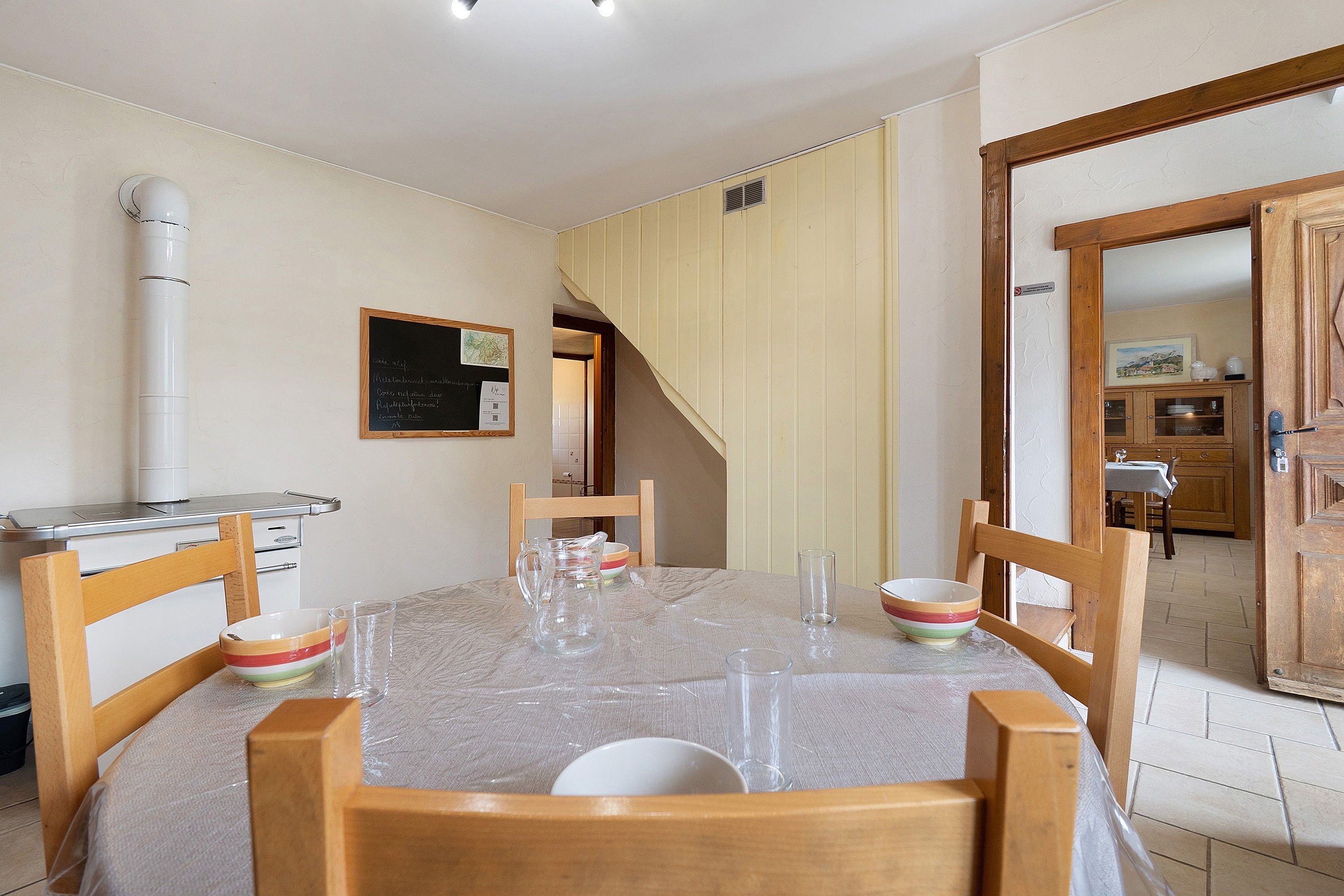 A dining area with a round table, chairs, a kitchen area, and a staircase leading to another room.