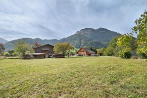 Un paisaje rural con dos casas de madera, un campo cubierto de césped y una montaña al fondo.