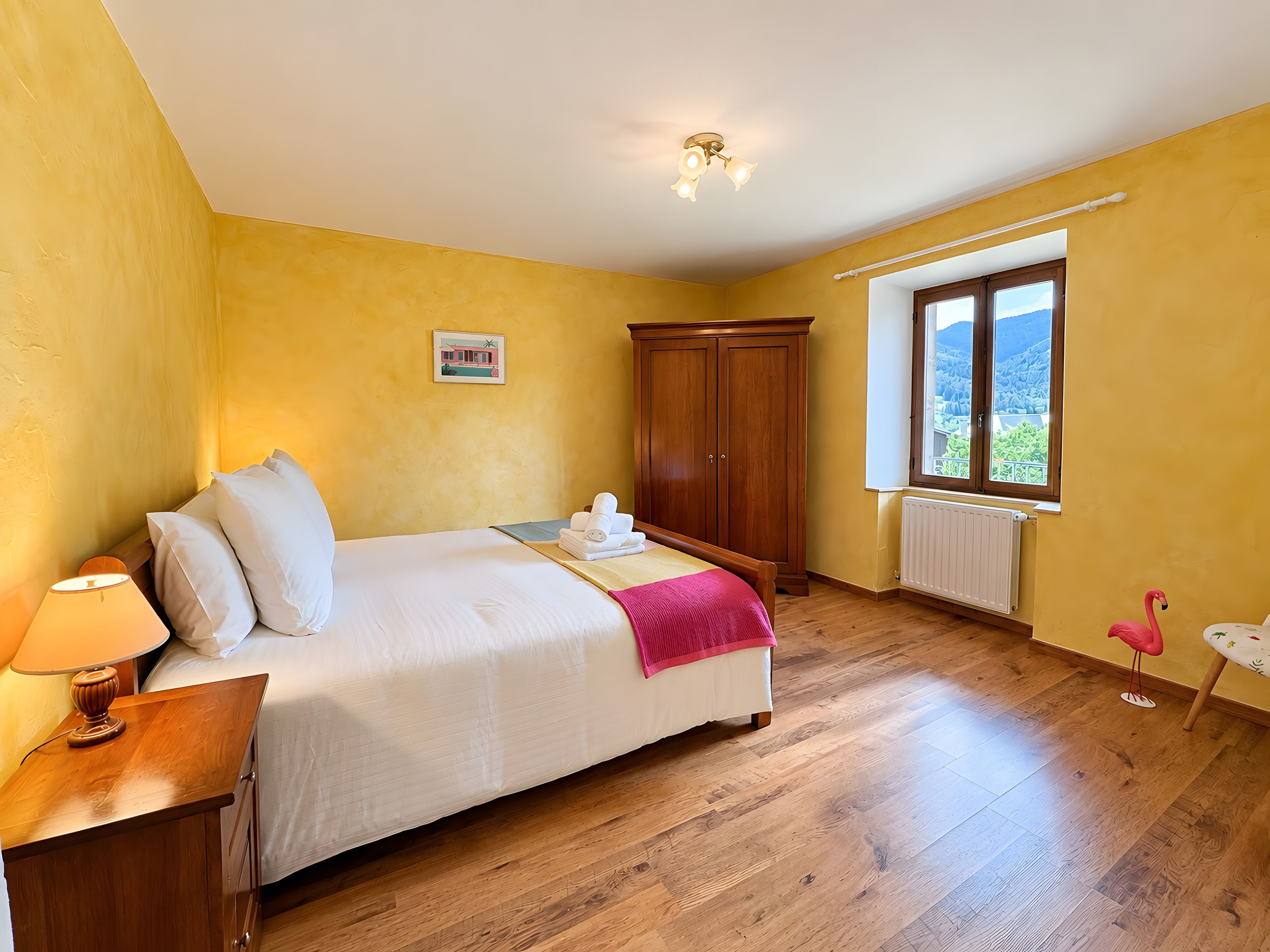 Une chambre à coucher avec un lit, une armoire en bois, une table de chevet, une lampe et une fenêtre donnant sur un beau paysage.