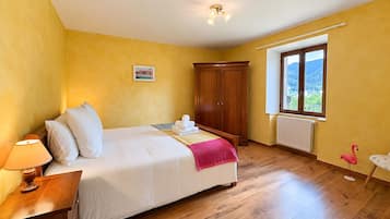 Une chambre à coucher avec un lit, une armoire en bois, une table de chevet, une lampe et une fenêtre donnant sur un beau paysage.