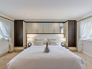 A bedroom with a large bed, two bedside tables, a nightstand, a dresser, and a mirror. - 4 Bed in Bideford (oc-nilga) (Bideford)