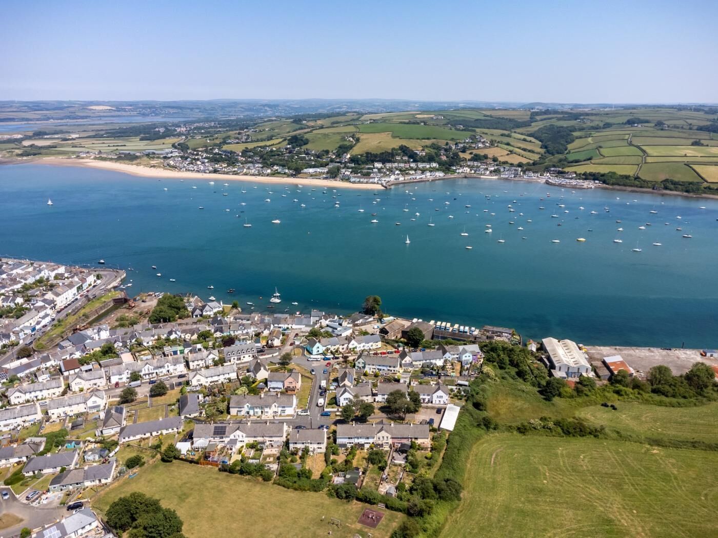 An aerial view of a coastal town with residential areas, a sandy beach, and numerous boats in the water.