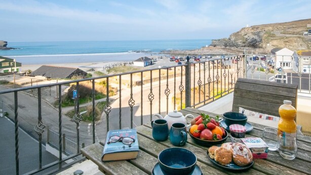 A balcony with a view of the beach, a book, a teapot, cups, a fruit bowl, and a bottle of juice. - 2 Bed in Redruth (oc-sanap) (Portreath)