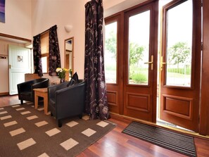 Ein Zimmer mit Holztür, Schreibtisch, Stuhl, Teppich und einem Fenster mit Vorhängen.