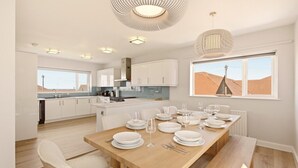 Una cocina moderna con armarios blancos, una mesa de madera dispuesta para seis comensales y un ventanal con vistas al paisaje desértico.