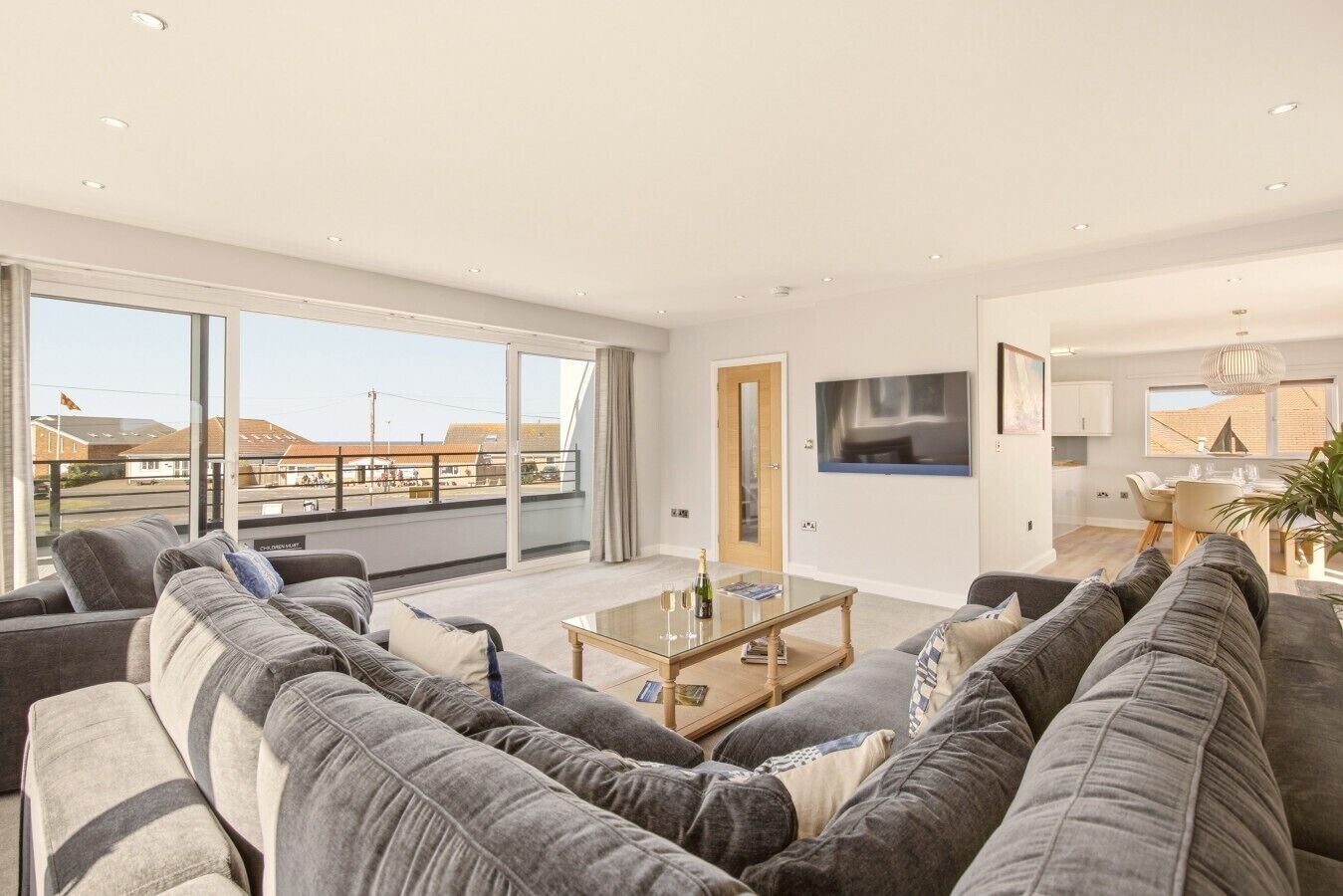 Een moderne woonkamer met een grote zithoek, een glazen salontafel en een aan de muur bevestigde televisie.