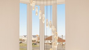 Una habitación moderna con un ventanal grande, lámparas colgantes y vistas a un barrio residencial.