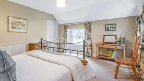 Quarto com uma cama, uma mesa, uma cadeira, um radiador e uma janela com cortinas.