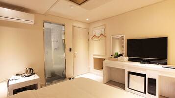 A hotel room with a bed, a TV, a minibar, a shower, and a desk with a kettle.