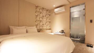 A hotel room with a large bed, a bedside table with a lamp, an air conditioning unit, and a glass-enclosed shower.