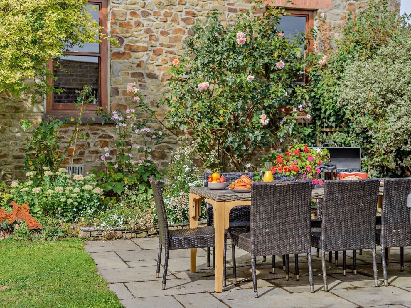 An outdoor patio with wicker furniture, a table with fruits and a beverage, and a stone building in the background.