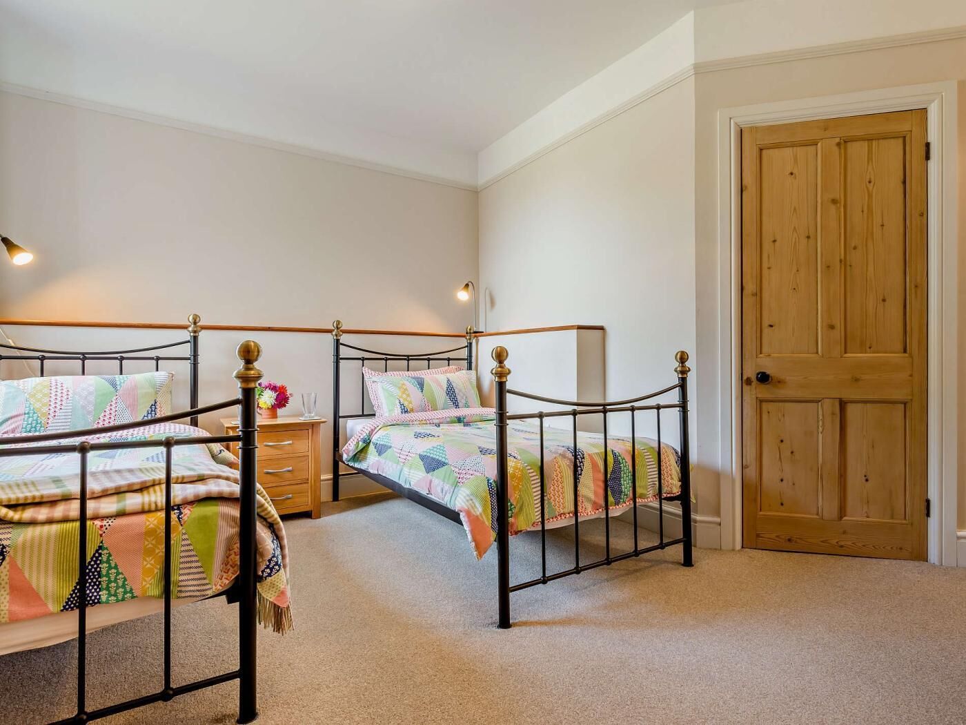 A bedroom with two single beds, a wooden door, and a nightstand with a lamp.