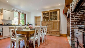 A kitchen with a dining table, chairs, cabinets, and a brick wall. - 4 Bed in Bude (oc-ssham) (Stratton)