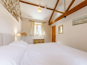 Ein Schlafzimmer mit einem Bett, einem Vorhangfenster, einer Holzbalkendecke und einer Wandleuchte.