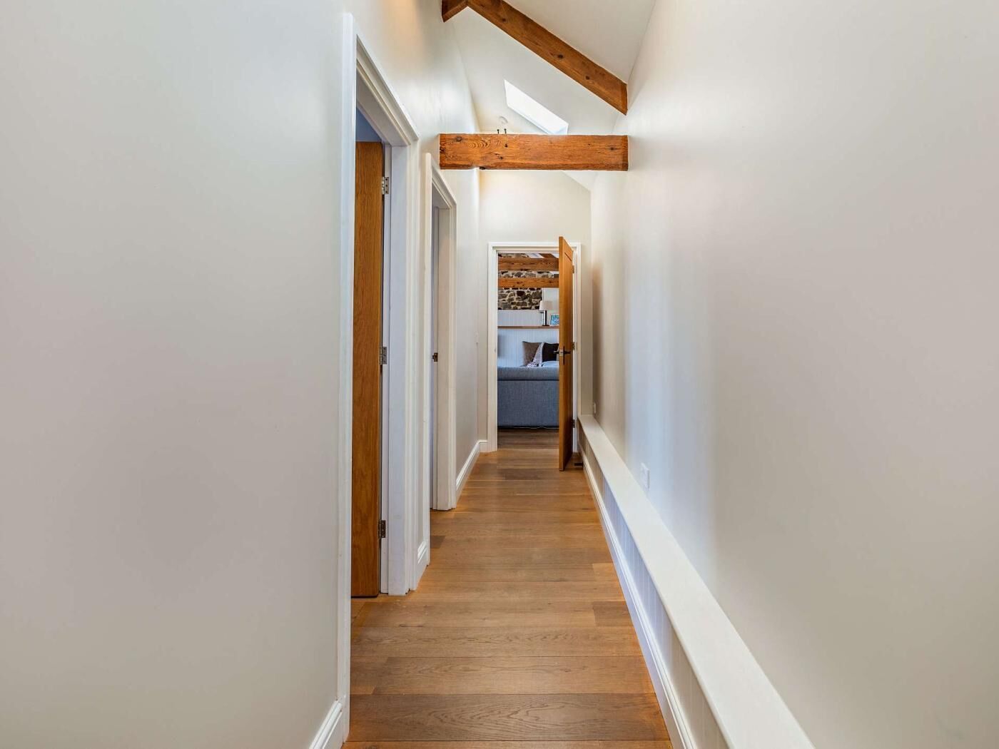 Un couloir étroit, doté de planchers en bois et de murs blancs, qui mène à une chambre à coucher avec un lit et une commode.