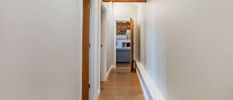 Un couloir étroit, doté de planchers en bois et de murs blancs, qui mène à une chambre à coucher avec un lit et une commode.