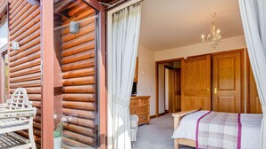 Une chambre située dans une cabane en rondins, avec un lit, une commode et une porte en bois donnant sur une autre pièce.
