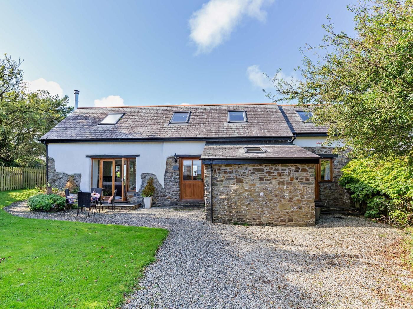 A house with a stone exterior, a gravel driveway, and a small garden with a table and chairs.