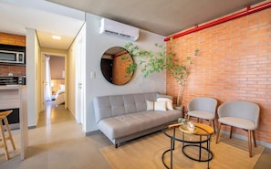 A modern living room with a sofa, two chairs, a round table, a potted plant, and a brick wall.