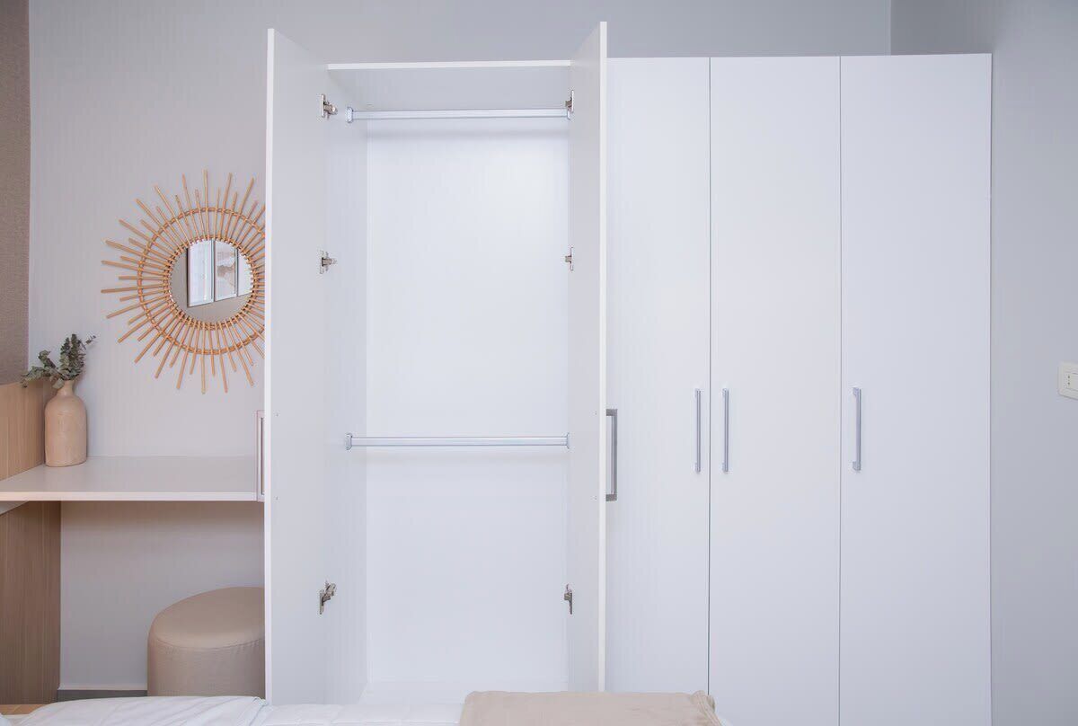 A bedroom with a bed, a wardrobe, a mirror, and a small stool.
