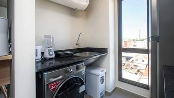 A compact kitchen with a washing machine, a coffee maker, and a sink.