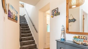 A staircase with a handrail, a wall-mounted sign reading 'HALEWA NORTH SHORE,' and a decorative lighthouse on a console table. - 5 Bed in Bideford (oc-09156) (Northam)