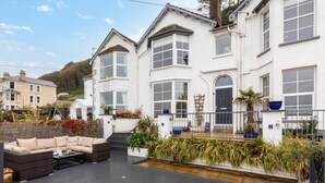 A white building with a covered patio area, outdoor seating, and potted plants. - 5 Bed in Bideford (oc-09156) (Northam)