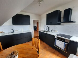 A modern kitchen with black cabinets, a white countertop, and a wooden dining table. - Apartment in a half-timbered house with a unique garden. Golf Course, Steinhuder Meer. (Rehburg-Loccum)