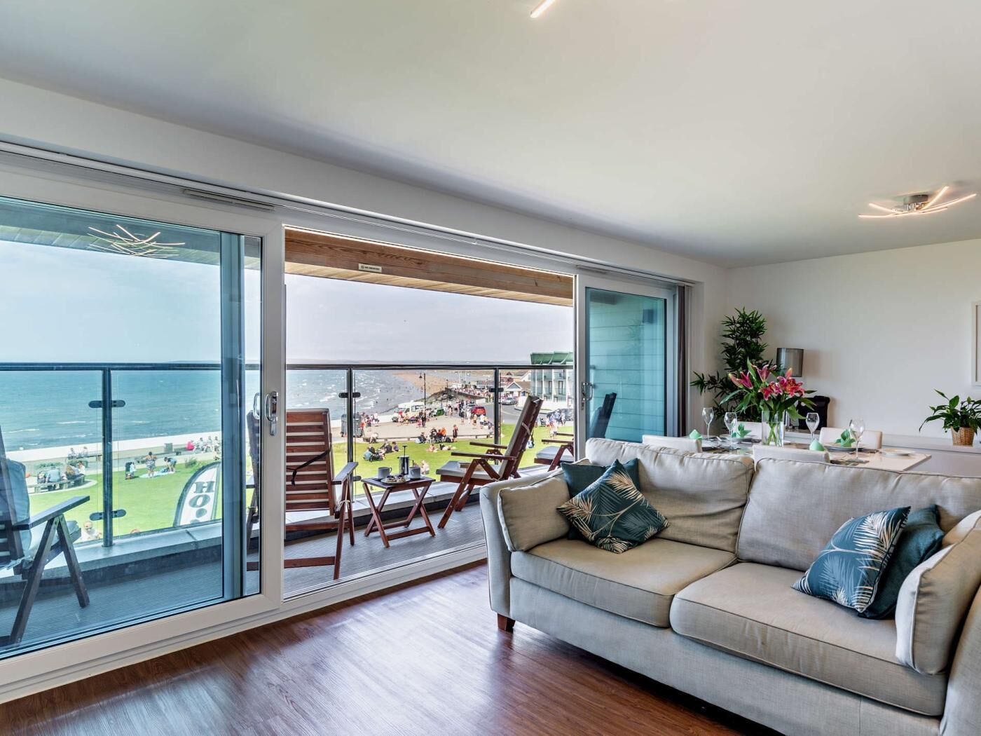 A spacious living room with a large sliding glass door leading to a balcony overlooking a beach.