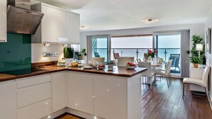 A modern kitchen with white cabinets, a wooden countertop, and a view of the sea through large windows. - 2 Bed in Bideford (oc-sscpe) (Westward Ho!)