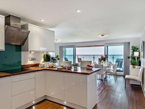 A modern kitchen with white cabinets, a wooden countertop, and a view of the sea through large windows. - 2 Bed in Bideford (oc-sscpe) (Westward Ho!)