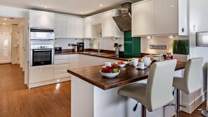 A modern kitchen with white cabinetry, a wooden countertop, and a central island with seating. - 2 Bed in Bideford (oc-sscpe) (Westward Ho!)