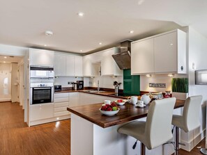 A modern kitchen with white cabinetry, a wooden countertop, and a central island with seating. - 2 Bed in Bideford (oc-sscpe) (Westward Ho!)