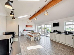 A modern kitchen with white cabinets, a dining area with a wooden table and chairs, and a large sliding glass door leading to a balcony. - 11 Bed in Bideford (oc-redla) (Instow)