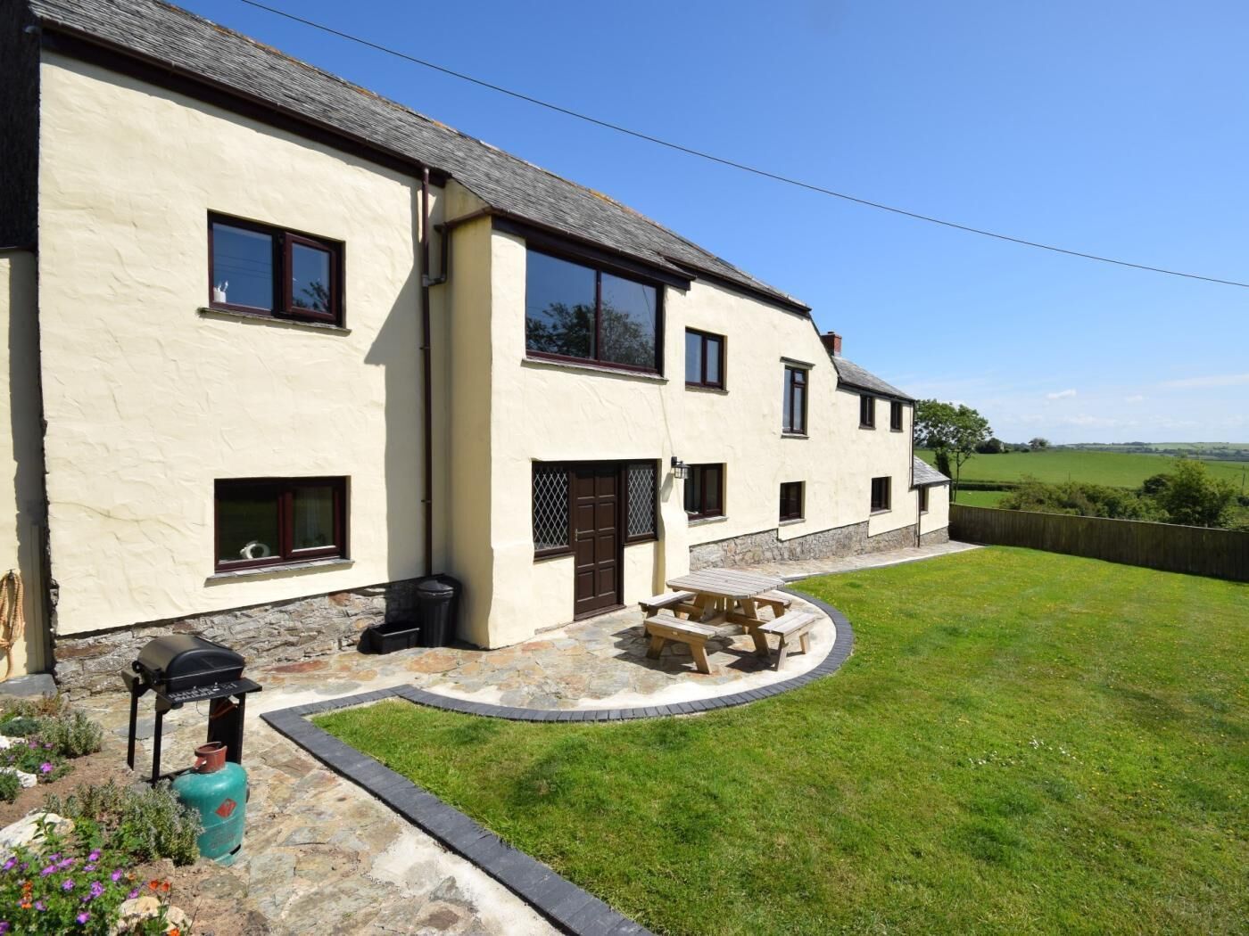 A two-story house with a stone foundation, a small patio with a barbecue, and a grassy yard.