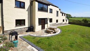 A two-story house with a stone foundation, a small patio with a barbecue, and a grassy yard. - 2 Bed in Bideford (oc-infpb) (Westleigh)
